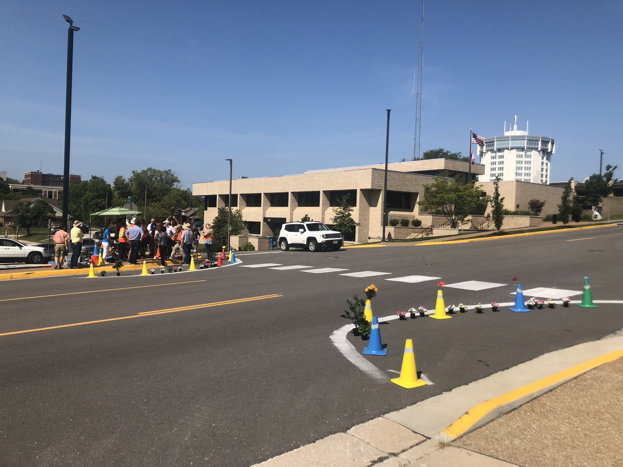 A community tactical-urbanism demonstration with a temporary curb extension, cones, and planters at a street crossing